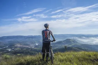 Man with bicycle helmet admires the view of the mountainous valley in Austria on his bike holiday with the mountain bike from a green meadow