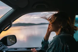 A woman on the front passenger seat of a camper. She smiles and her hair flies in the wind. In the background of sunset.
