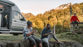 3 Männer, die vor einem Grand California sitzend ihr Essen genießen