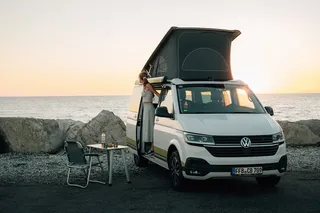 A camper is on a coast. A woman leans out of the door.